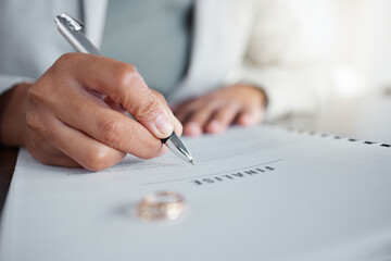 Signature, ring and divorce paper of a woman at table with legal paperwork, anxiety or documents. Female person sign with pen on papers with wedding band jewellery for separation, cheating or mistake