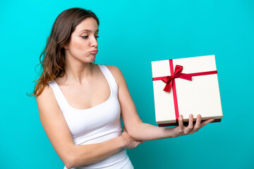 Young caucasian woman holding a gift isolated on blue background with sad expression