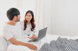 © PHAISITSAWAN - Young happy asian couple using laptop in bed watching movie, romantic time to enhance family relationship, family concept.