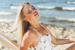 © rogerphoto - Happy blonde woman relaxing on a wooden deck chair at the ocean beach