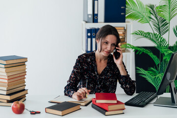 a woman in the office at the computer with a book speaks on the phone work online business finance