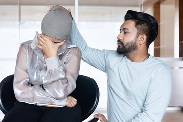 Sad and depressed south asian woman cancer patient with concealing head scarf, suffering from serious hair loss due to chemotherapy negative side effect but having family staying together for support