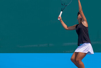 A girl plays tennis on a court with a hard blue surface on a summer sunny day