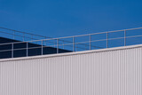 Fototapeta Na sufit - Modern white and black corrugated steel factory buildings wall with aluminium fence on rooftop against blue sky background 