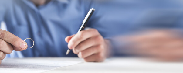 Wall Mural - Man holding a wedding ring and signing divorce contract.