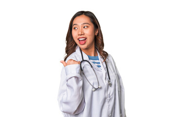 A young asian doctor woman points with thumb finger away, laughing and carefree.