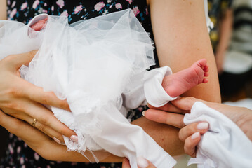 Baptism ceremony of a baby. Close up of tiny baby feet, the sacrament of baptism. The godfather holds the child in his arms. Priest and godmother stretch hands to child legs. Temple, Orthodoxy.