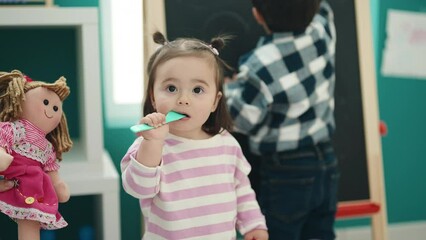 Poster - Adorable boy and girl preschool students drawing on blackboard sucking fork toy at kindergarten