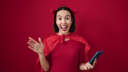 Sticker - Young beautiful hispanic woman wearing devil costume using smartphone over isolated red background