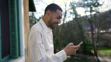one happy arab young man liking message on cellphone while standing outside at balcony. a middle eas