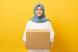 Young asian muslim woman holding parcel box for ramadan charity isolated over orange background. charity alms concept.