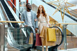 © Roman - young beautiful red-haired girl and african bearded guy get pleasure from buying goods, clothes, presents, gifts on holidays, escalator in the background of the photo