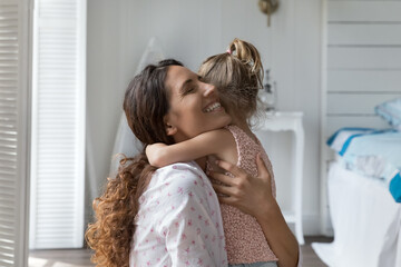 Wall Mural - Happy loving mother hugging little kid with closed eyes, tightening daughter girl with affection, devotion, happiness, enjoying motherhood, close relations, bonding with child