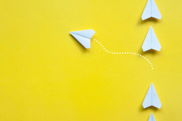 Wall Mural - Top view of white paper airplane origami leaving other white airplane on yellow background with customizable space for text or ideas. Copy space.