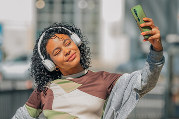 Wall Mural - latin girl with afro hair with headphones and mobile phone in the street