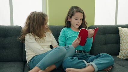 Sticker - Adorable girls reading book sitting on sofa at home