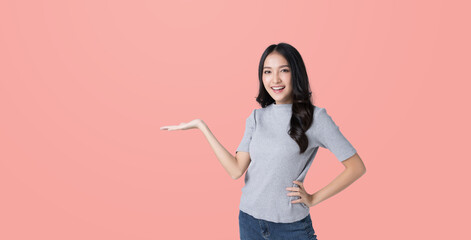 Wall Mural - Young Asian woman opeing hand to empty space and looking hand isolated pink color background