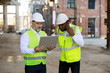 © sakoqwakestock - Caucasian senior foreman with wireless laptop discussing about all peculiarities of project to african american male architect at construction area. Concept of business meeting and building process.
