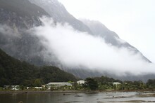 Village With Green Vegetation And Mountains Covered In Clouds. Milford Sound, New Zealand.