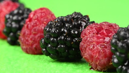 Wall Mural - Blackberries and raspberries with water drops on a green background. Movement from the lower right corner to the upper left corner. Side view. Loop motion. Rotation 360. 4K UHD video footage 3840X2160