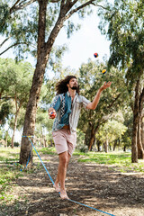 Wall Mural - Confident young man juggling and balancing on the slackline in city park