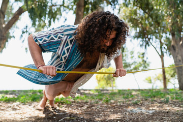 Wall Mural - Confident young man doing pushups and balancing on the slackline in city park