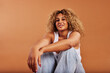 © Flamingo Images - Smiling woman wearing a tank top and jeans sitting on an orange background