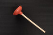 Red toilet plunger with wooden handle isolated on black background. Professional plumber tool.