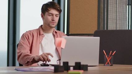 Wall Mural - attractive young employee sits down at the desk, puts on glasses and starts working on the laptop