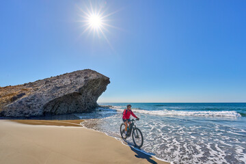 Wall Mural - nice senior woman cycling with her electric mountain bike in the volcanic nature park of Cabo de Gata, Costa del Sol, Andalusia, Spain