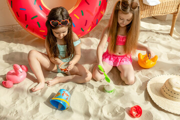 Creative little girls having fun together on beach sand. Two adorable young friends smiling happily while playing with each other at the beach. Cheerful kids enjoying their summer vacation.