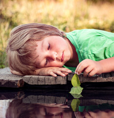 Wall Mural - green leaf-ship in children hand in water, boy in park play with boat in river