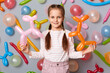© sementsova321 - Charming calm little girl  with pigtails standing against gray decorated wall holding multicolored balloons in hands, being in festive mood.