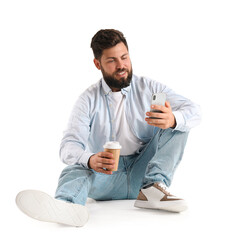 Canvas Print - Young bearded man with cup of coffee using mobile phone on white background