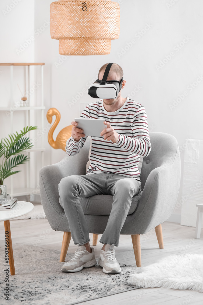 Young man with VR glasses and tablet computer at home