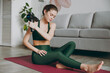 © ViDi Studio - Full body young athletic fitness trainer instructor woman wear green tracksuit using percussion massager for body shoulder hand muscles, hand gun train do exercises at home gym Workout sport concept.