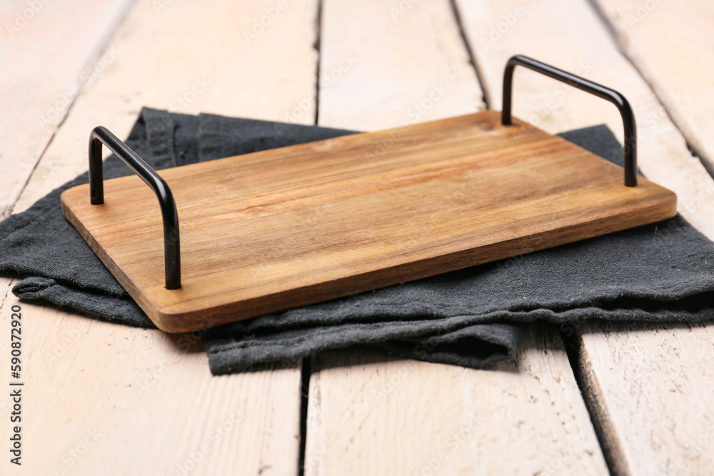 Cutting board with handles and napkin on light wooden background, closeup
