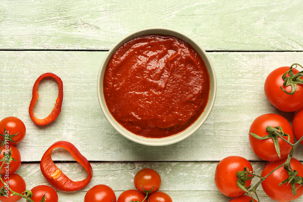 Bowl with tasty tomato paste and fresh vegetables on light wooden background