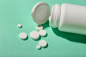 Bottle with white pills on green background, closeup