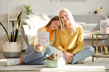 Young woman greeting her mother with card at home