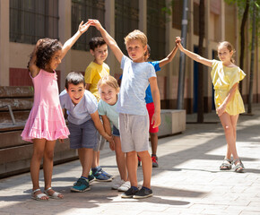 Wall Mural - Group of positive schoolchildren holding hands up and playing together in park