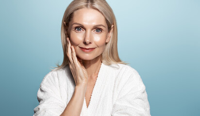 Wall Mural - Elegant middle aged woman, head and shoulders with glowing skin, nourished, moisturized face and body, smiling at camera, blue background