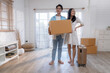 Asian couple carry a large cardboard box into the new home.