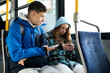 © Oleksandra - two teenagers in blue clothes sit on a bus Canada Vancouver hoods autumn winter spring tracksuits use a mobile phone search for geolocation travel travelers real life Interior of crowded bus