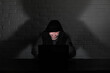 © alexkich - Hacker in black mask and hood at the table