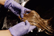© Татьяна Волкова - Cropped photo of woman hairdresser hairstylist beautician wearing blue rubber gloves washing long dark hairpiece wig.