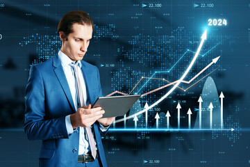 Poster - Attractive young businessman using tablet with growing business chart with arrow hologram on blurry office interior background. Business development to success and plan concept. Double exposure.