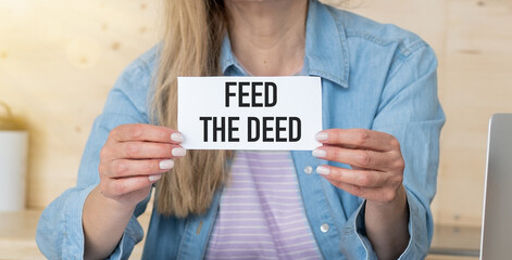 Wall Mural - FEED THE DEED message on a yellow card hold by a business woman, business concept image with soft focus background