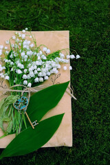 Wall Mural - Lily of the valley, key and old paper envelope in forest, green natural dark background. symbol of spring season. romantic spring composition with flowers. top view