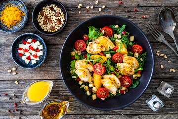 Wall Mural - Tasty Greek salad - fried chicken breast, halloumi cheese, oranges, pine nuts, raisins, mini tomatoes and fresh green vegetables on wooden background
